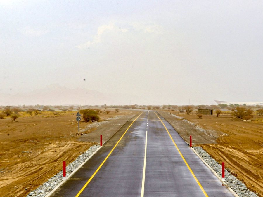 The completed Manah link road carriageway with new lane markings, running towards the Hajar mountains