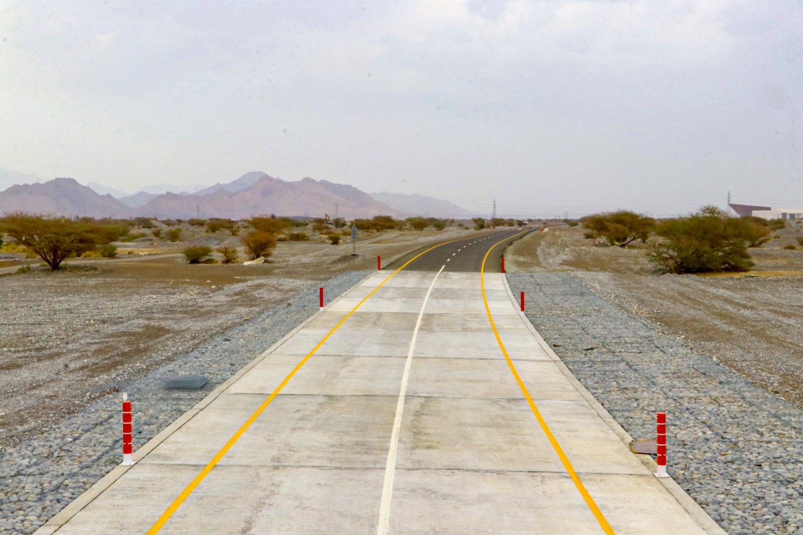 Concrete pavement section at a wadi crossing, with stone slope protection and marker posts to either side