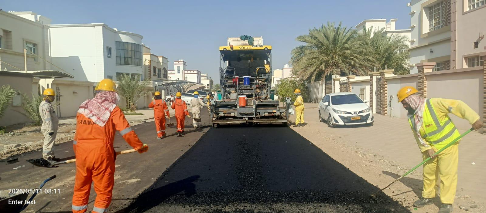 RRS-352 Muscat asphalt supply & laying — Vögele paver and Rawasi crew laying fresh asphalt surfacing on a Muscat residential street